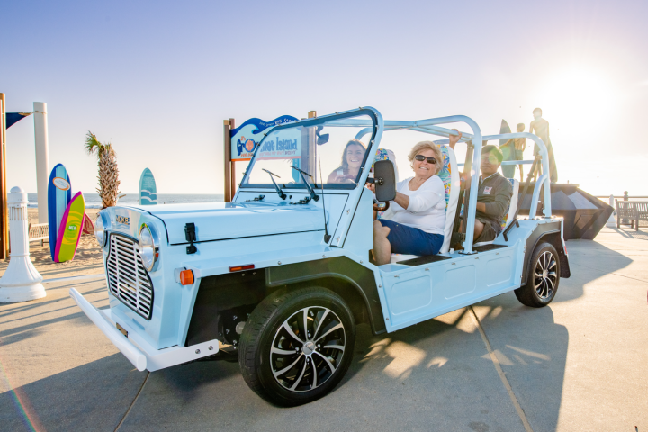 People in a blue open-sided vehicle near a beach.