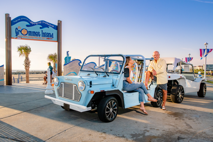 Two people with small cars near a beach entrance under a clear sky.