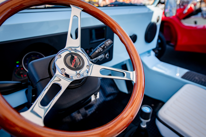 Vintage car interior with wood steering wheel and red and white accents.