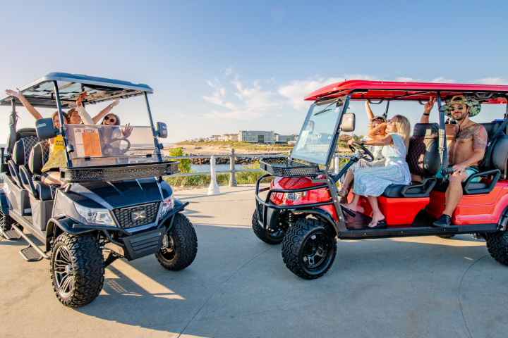 Two golf carts by the seaside, people inside enjoying the view on a sunny day.