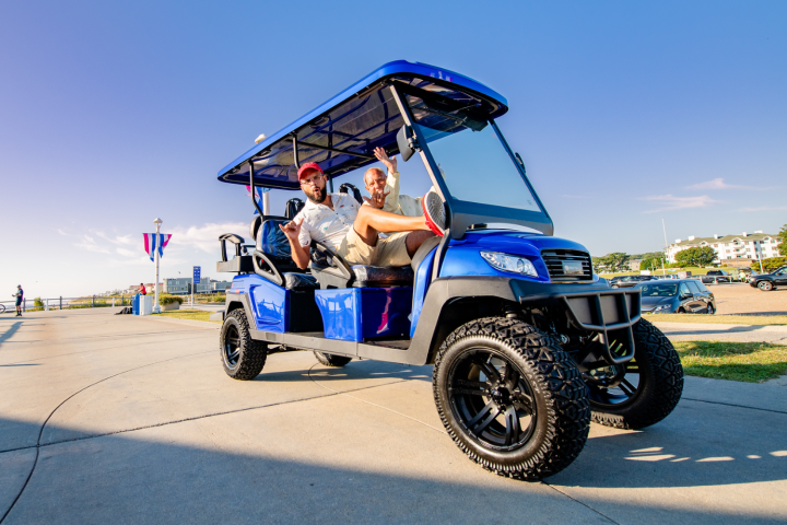 Two people smiling in a blue golf cart on a sunny day.