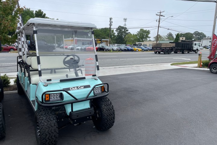Light blue golf cart parked on pavement near a street with cars.