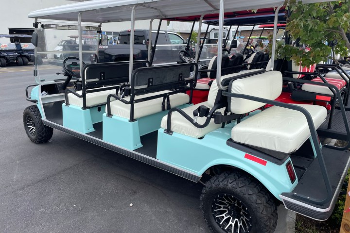 Light blue extended golf cart with white seats parked in a lot.