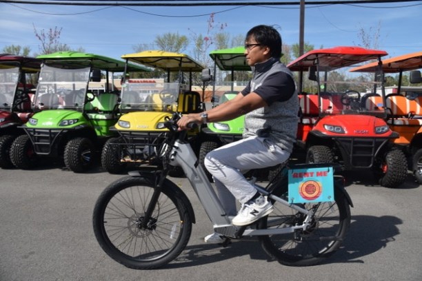 Person on a bike near colorful golf carts on a sunny day.