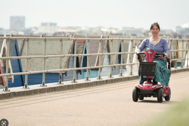 Person riding a red mobility scooter on a path near a railing.