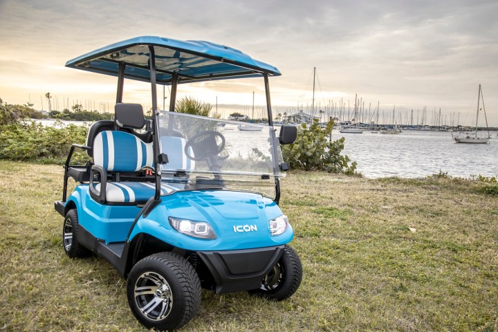 Blue golf cart parked on grass near a marina with sailboats.